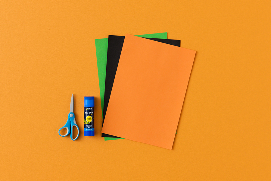 An overhead view of products that can be used to make a paper pumpkin lantern, including coloured paper, scissors and glue.