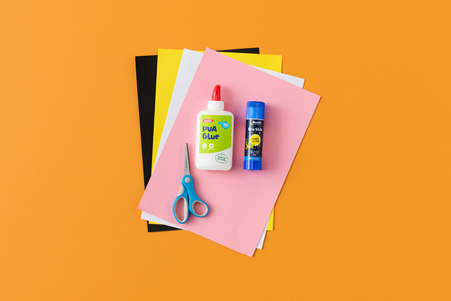 An overhead view of products that can be used to make a paper fan black cat, including black, yellow, white and pink coloured paper, scissors and glue.