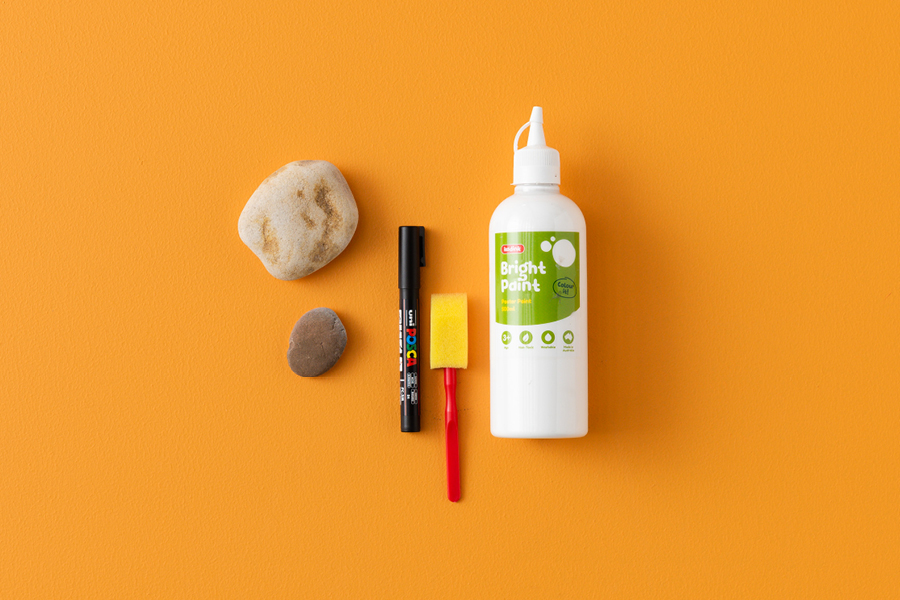An overhead view of products that can be used to make a ghostly paperweight rock, including a paint marker, paintbrushes and poster paint.