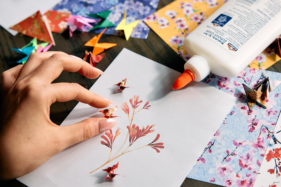 A close-up of one of Kiana’s artworks in progress. Kiana is placing origami butterflies onto a painting of red flowers.