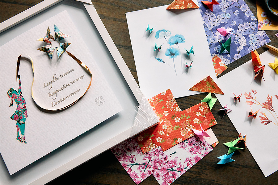A range of origami art, floral designs and colourful paper crafts arranged on a wooden table.