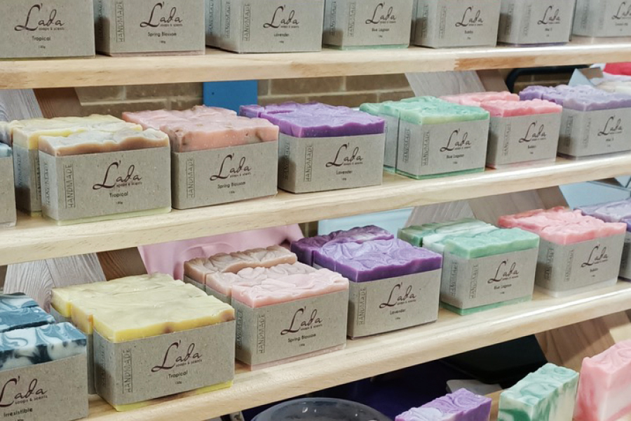 A multi-shelf display of L’ada soap bars in a variety of colours, including blue, yellow, pink, purple and green, and wrapped in a khaki-coloured paper product label.