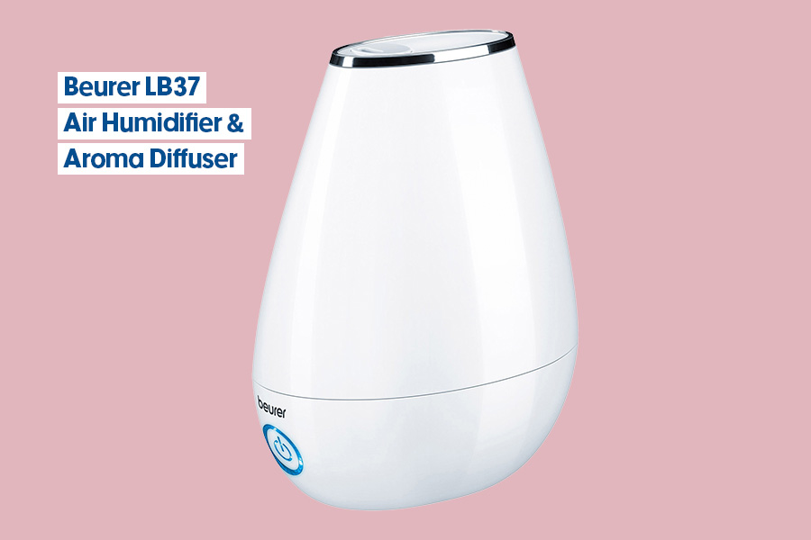 A Beurer LB37 air humidifier and aroma diffuser in a white teardrop-shaped design with a silver top and a blue power button, displayed against a pink background.