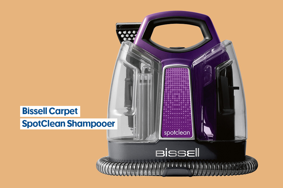 A Bissell Carpet SpotClean Shampooer in purple and black, featuring a compact design with a handle and transparent water tanks, set against an orange background.
