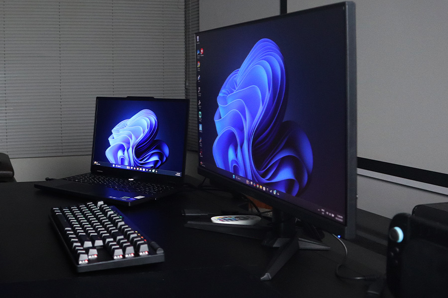 A gaming setup featuring a mechanical keyboard, a gaming laptop and a monitor both displaying abstract blue designs.