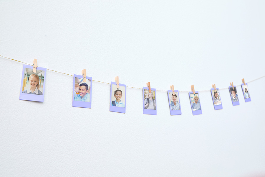 A string of purple-framed mini photos pegged to a twine line across a white wall, showing portraits of students.