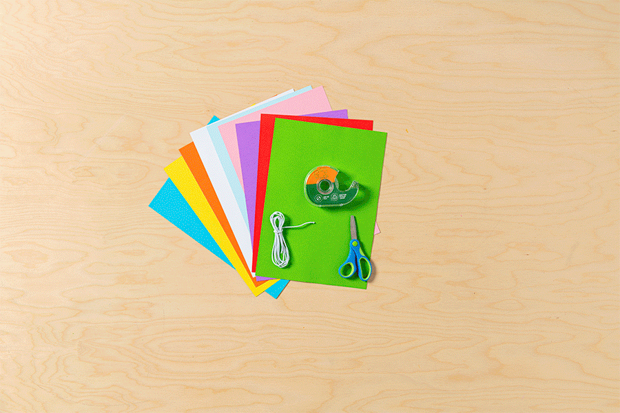 A series of images showing coloured paper being cut with scissors into strips, then looped and taped to create a bright paper chain garland shaped like an S.