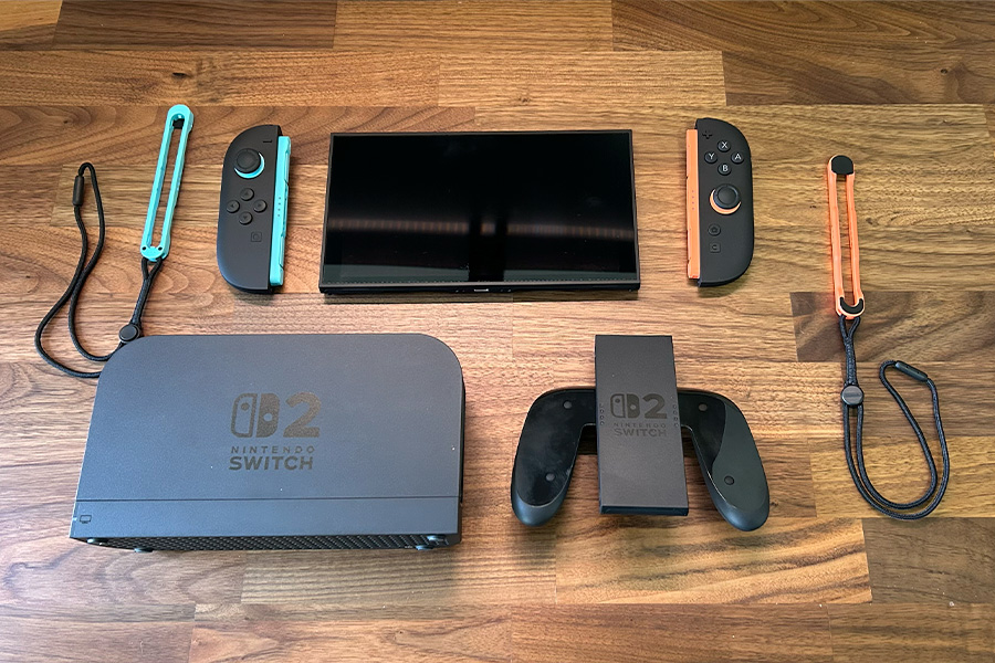 A disassembled Nintendo Switch 2 console laid out on a wooden surface, including Joy-Con 2 controllers, straps and grip, the console screen and dock.