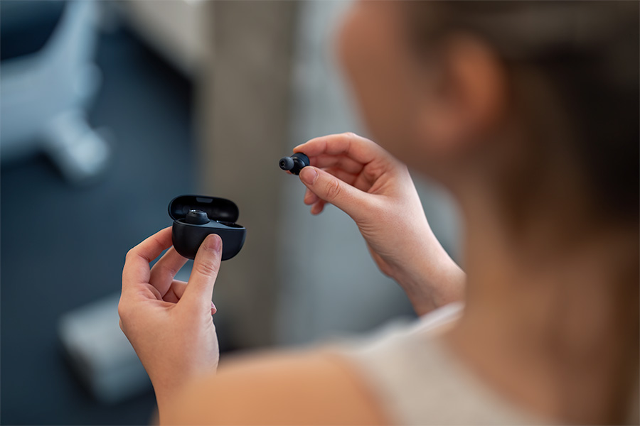 Close-up of a person at a gym holding a black wireless earbud and an open charging case.