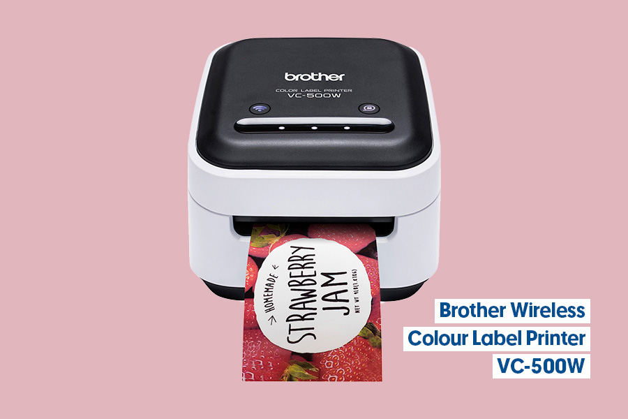 A Brother VC-500W wireless colour label printer printing a full‑colour ‘Strawberry Jam’ label, shown against a pink background.