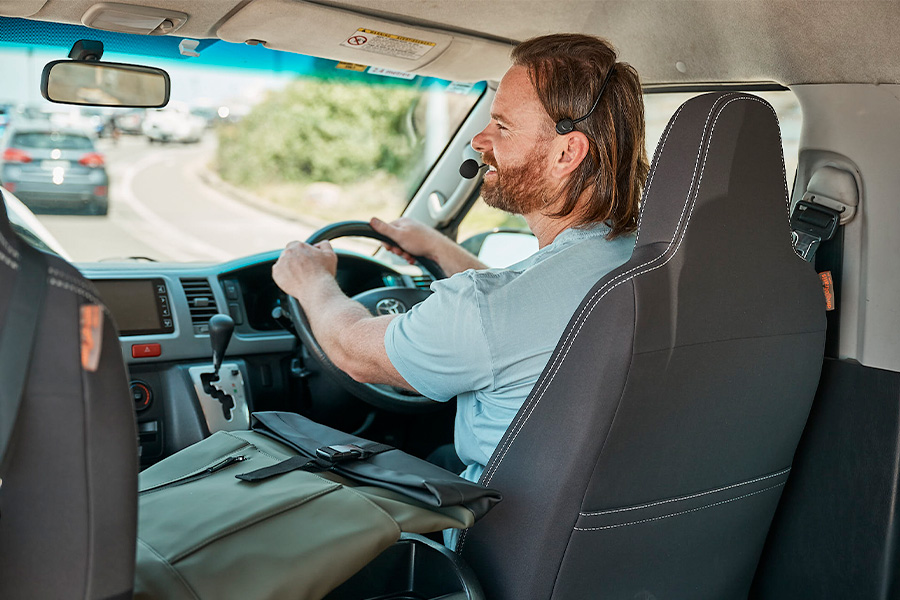 Nathan driving a tour van with a bag placed on the passenger seat and a view of the road ahead through the windshield.