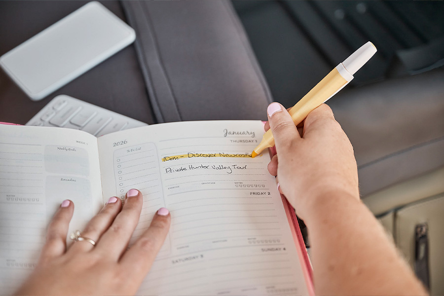 Close-up of hands using a week-to-view diary, highlighting ‘10am – Discover Newcastle’ for January 2026 with a yellow highlighter.