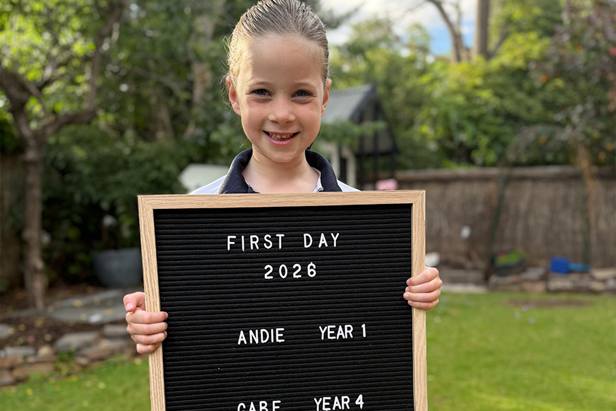 Andie holding a black felt memo letter board reading ‘FIRST DAY 2026 – ANDIE YEAR 1’ in a backyard garden.