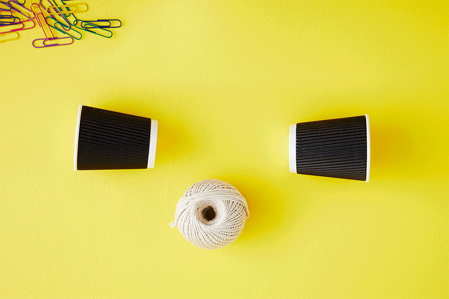 A series of images showing how to do a string phone STEM activity by making holes in two black paper cups using a pencil then attaching a long piece of string between them.