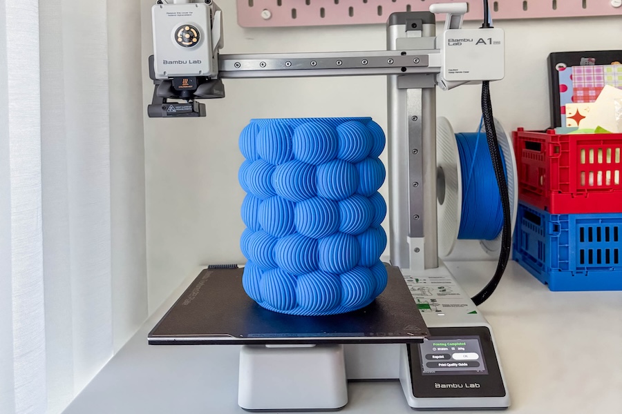 A blue printed 3D vase standing on the platform of the Bambu Lab A1 mini 3d printer, having just completed the printing process.