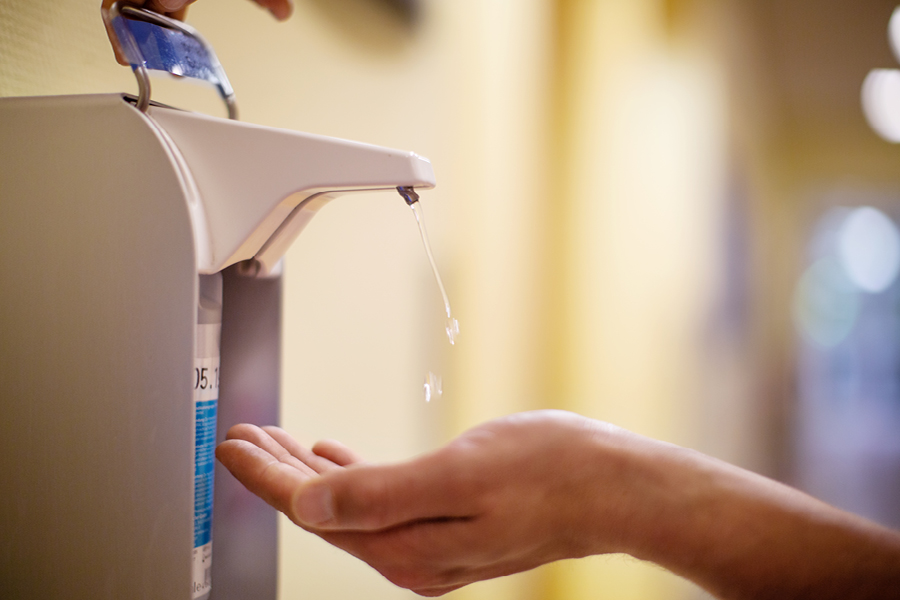  Wall-mounted hand sanitiser dispenser dripping liquid into an open palm.