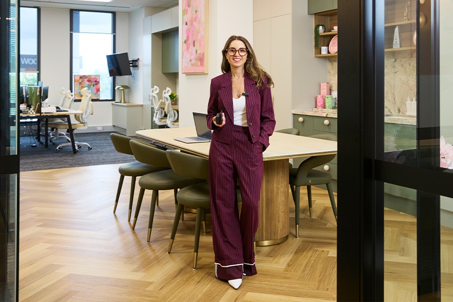 Renee leaning against a table with chairs in a kitchen within a modern office setting.