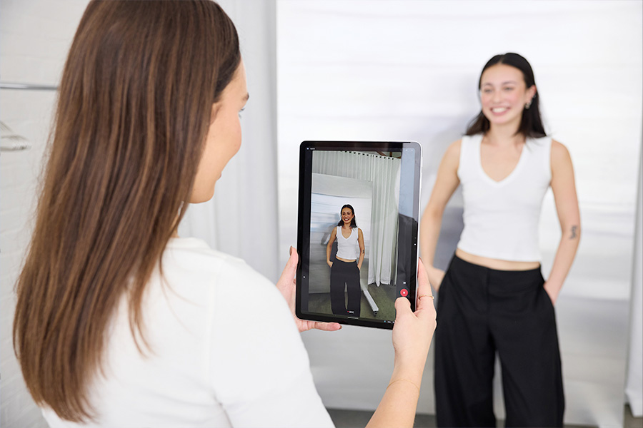 Kelsie using a Microsoft Surface Pro in tablet mode to record business partner Hanaka; the tablet screen shows them standing with hands in pockets in a studio.