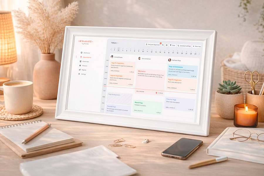 The Blaupunkt Smart Family Digital Calendar in a white frame displayed on a styled home desk with candles, notebooks and pens, and a succulent plant.