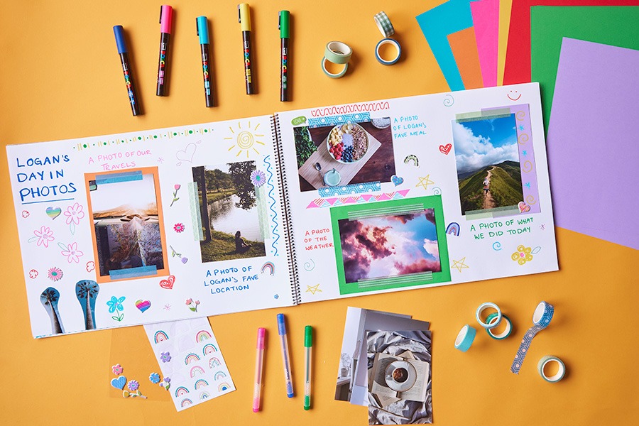 An open scrapbook on an orange surface with colourful pens, stickers, tape and photos arranged into a decorated memory page titled ‘Logan’s Day in Photos’.