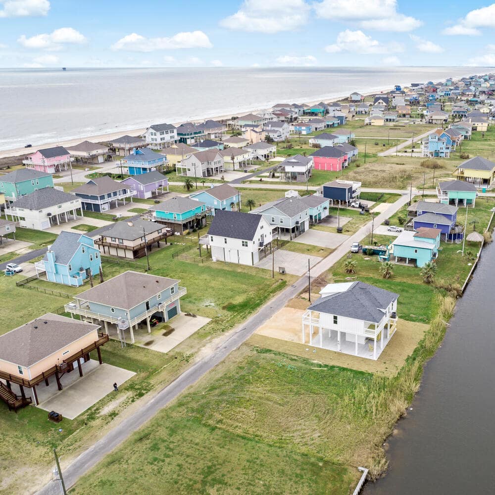 Aerial shot of houses in a strip of land with water on both sides, many houses have pillars and some are bright pastel colors