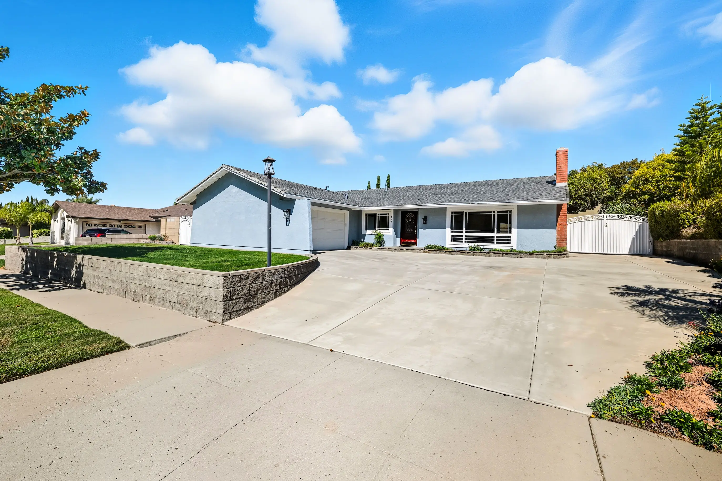 Modern elevated white house with wraparound porch and exterior staircase on gravel lot.