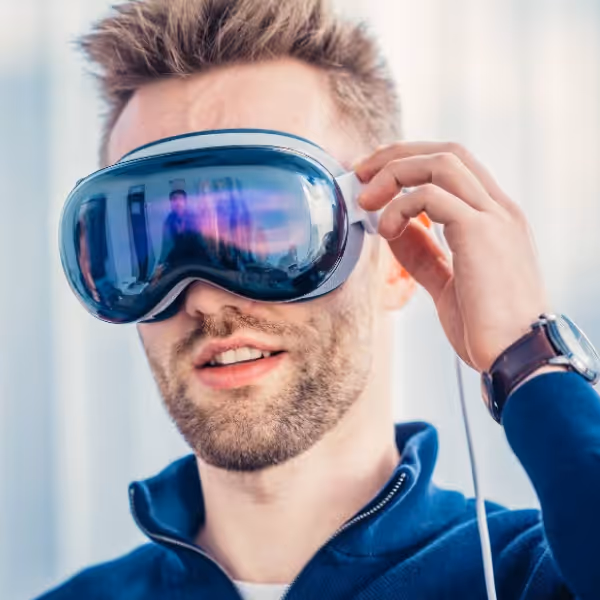 Man with light brown hair wearing a blue zip-up jacket and adjusting virtual reality headset.