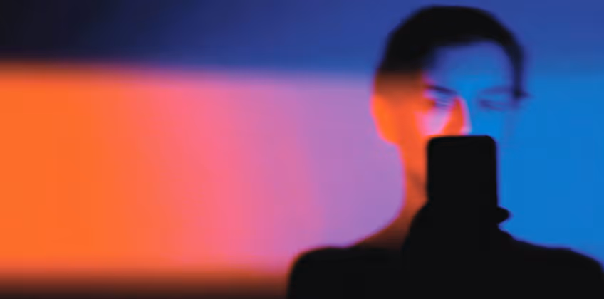 Blurred silhouette of a person holding a smartphone with a colorful gradient background of orange, pink, purple, and blue hues.