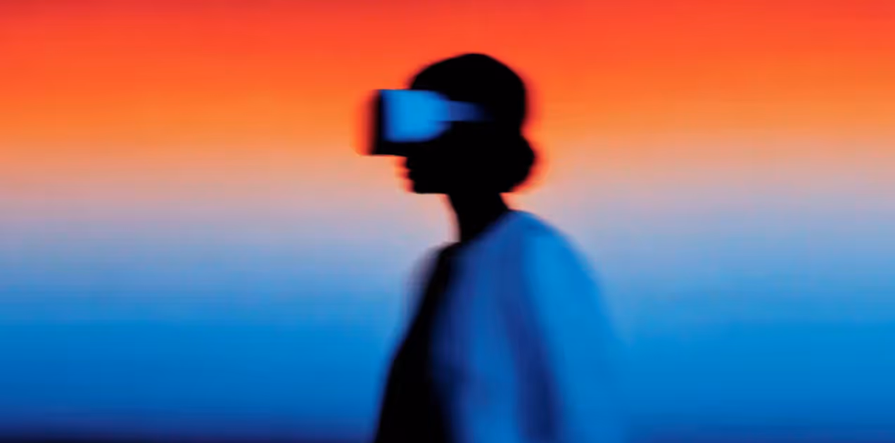 Blurred silhouette of a person wearing a virtual reality headset against a gradient orange to blue background.