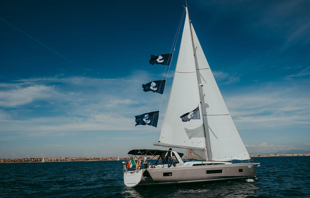 Uno yacht a vela con 4 bandiere con il logo di Beneteau naviga lungo la costa.