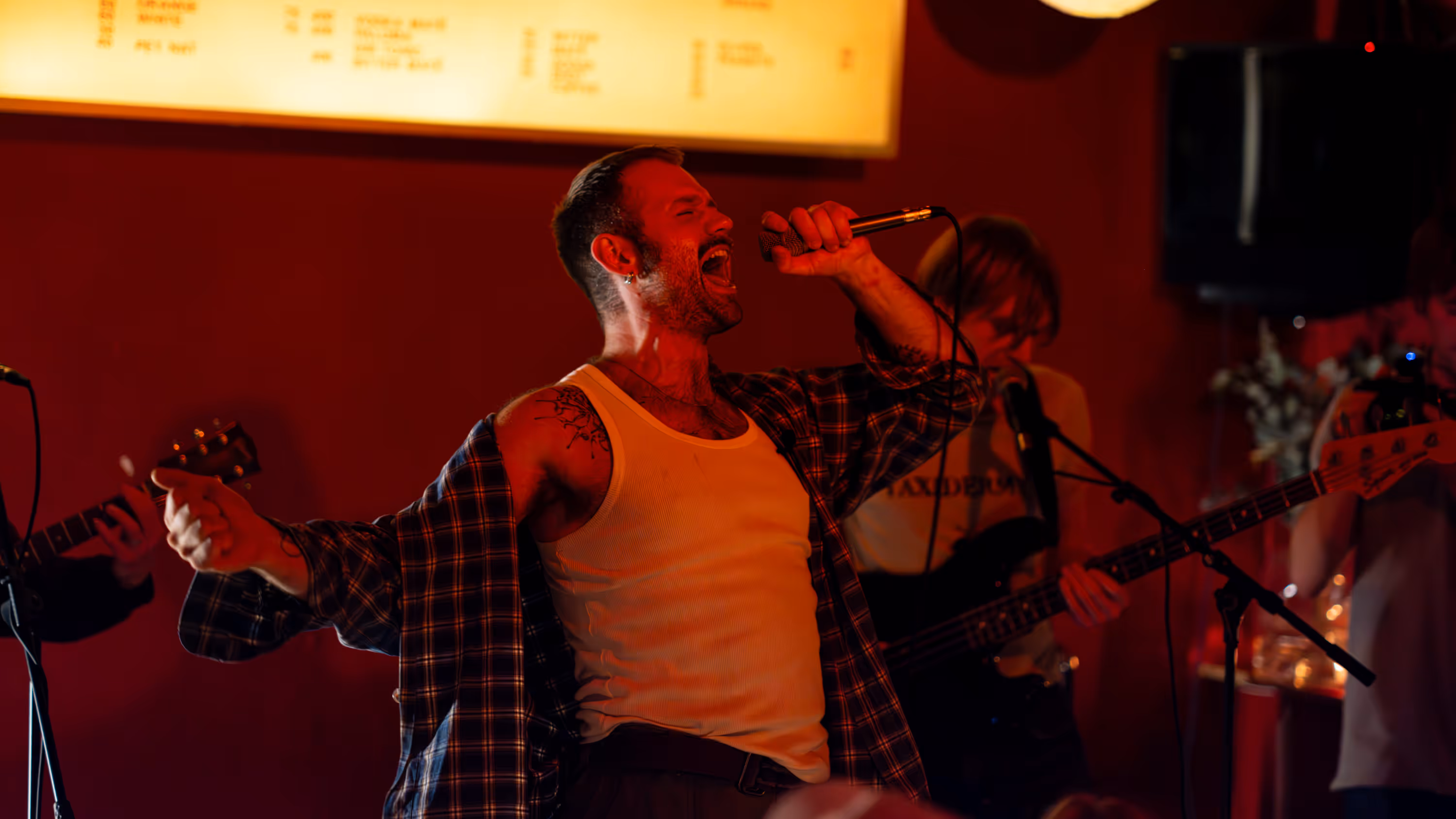 Male singer passionately performing with a microphone on stage in a dimly lit venue accompanied by a bass guitarist.