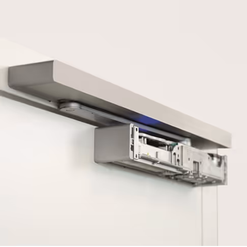 Grey door operator above a white door with the cover slid off exposing the drive unit - Easy Assist technology.