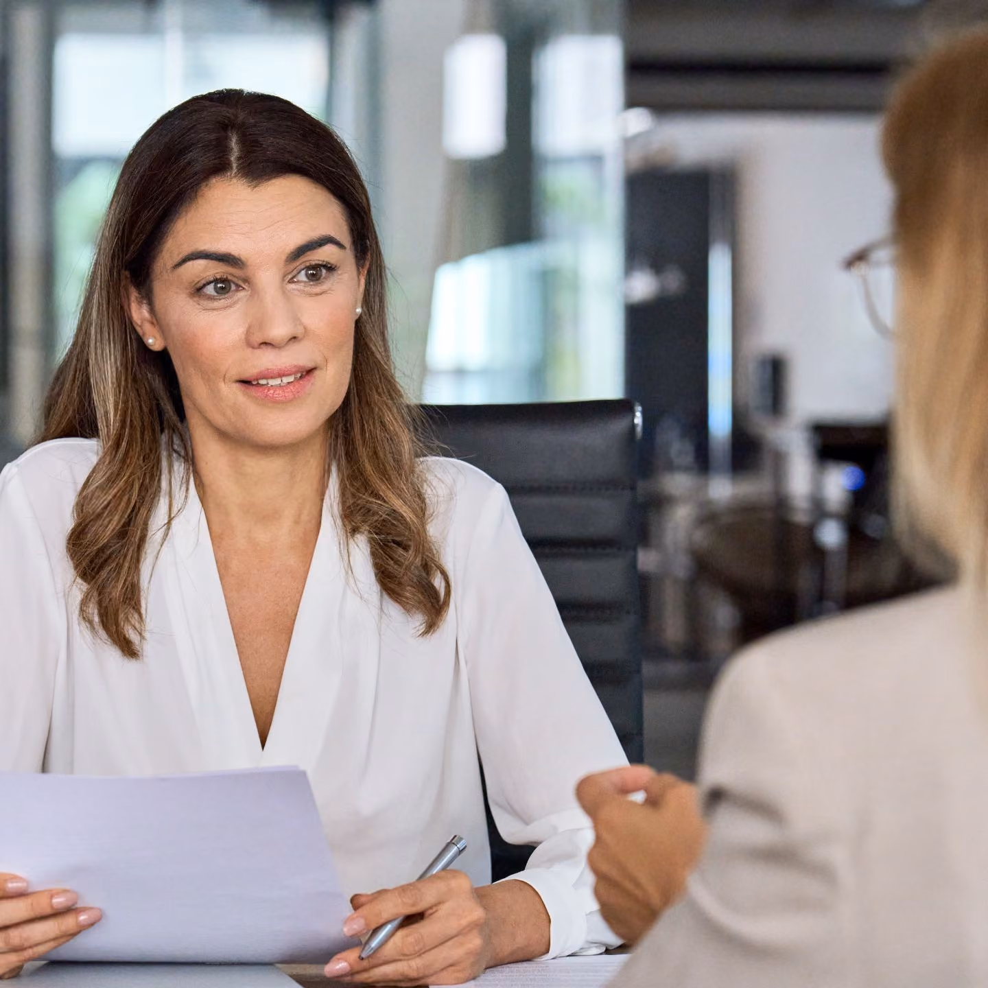 Two women in conversation across a desk in a modern office - dormakaba vacation rental contact.