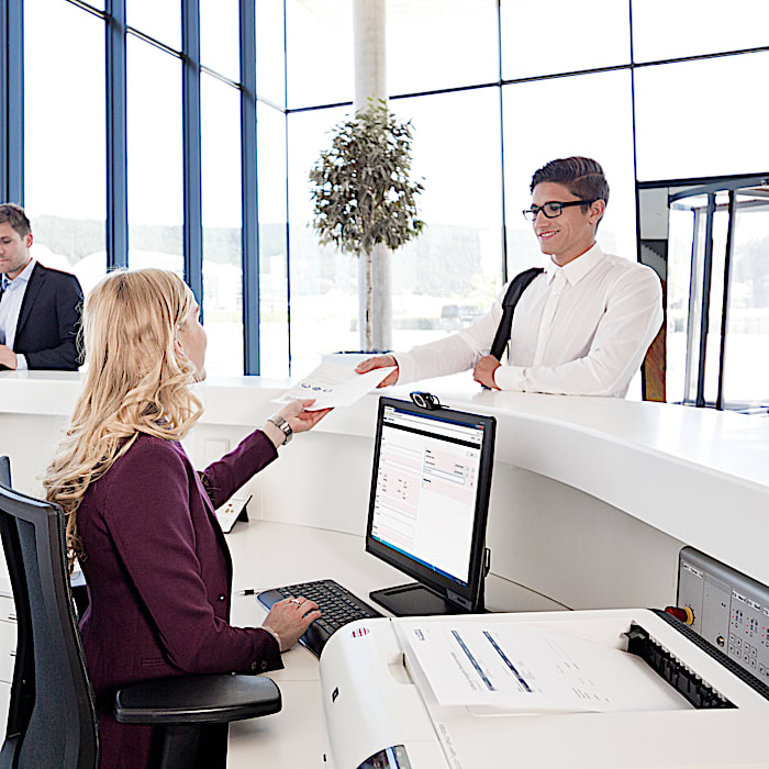 Reception desk with exos visitor management running on screen, showing exos 9300 in use at a building entrance.