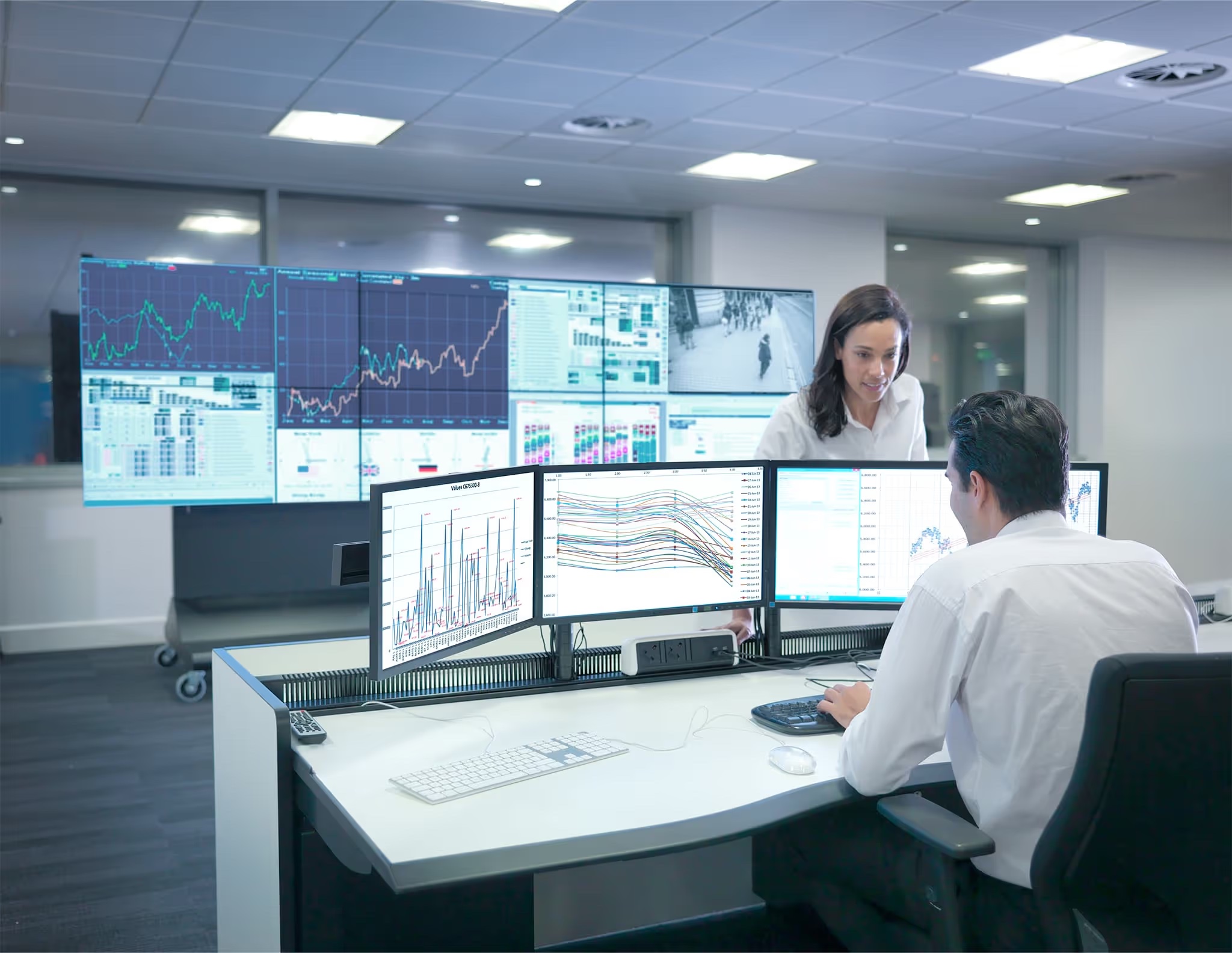 Two colleagues monitoring a building control room with wall displays and multi-screen dashboards, illustrating the central monitoring Connector ONE makes possible.