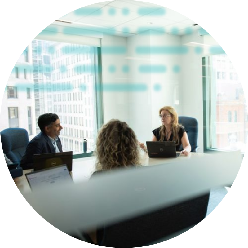 Woman standing between 2 men talking at a table with a computer and tablet