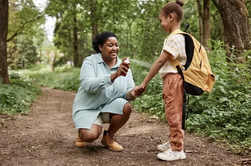A lady spraying insect repellent on a child