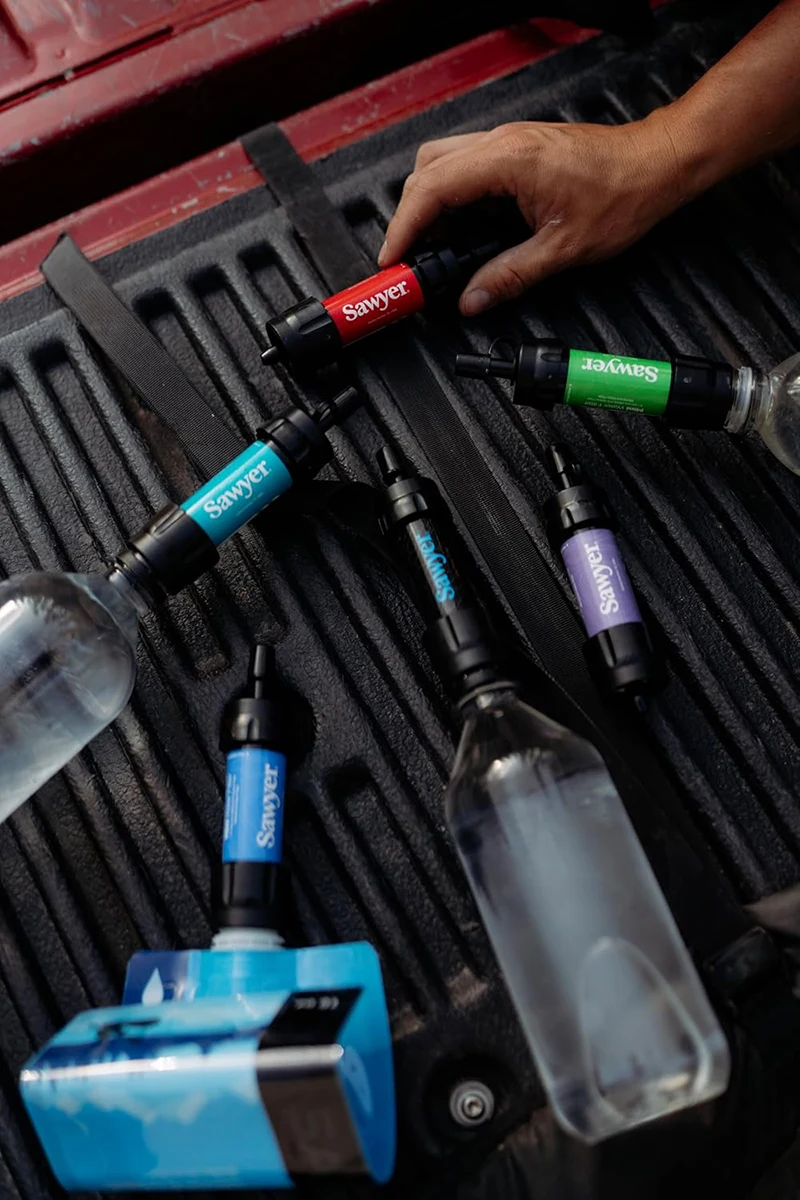 Several multi colored Sawyer mini water filters on truck bed with hand grabbing red filter