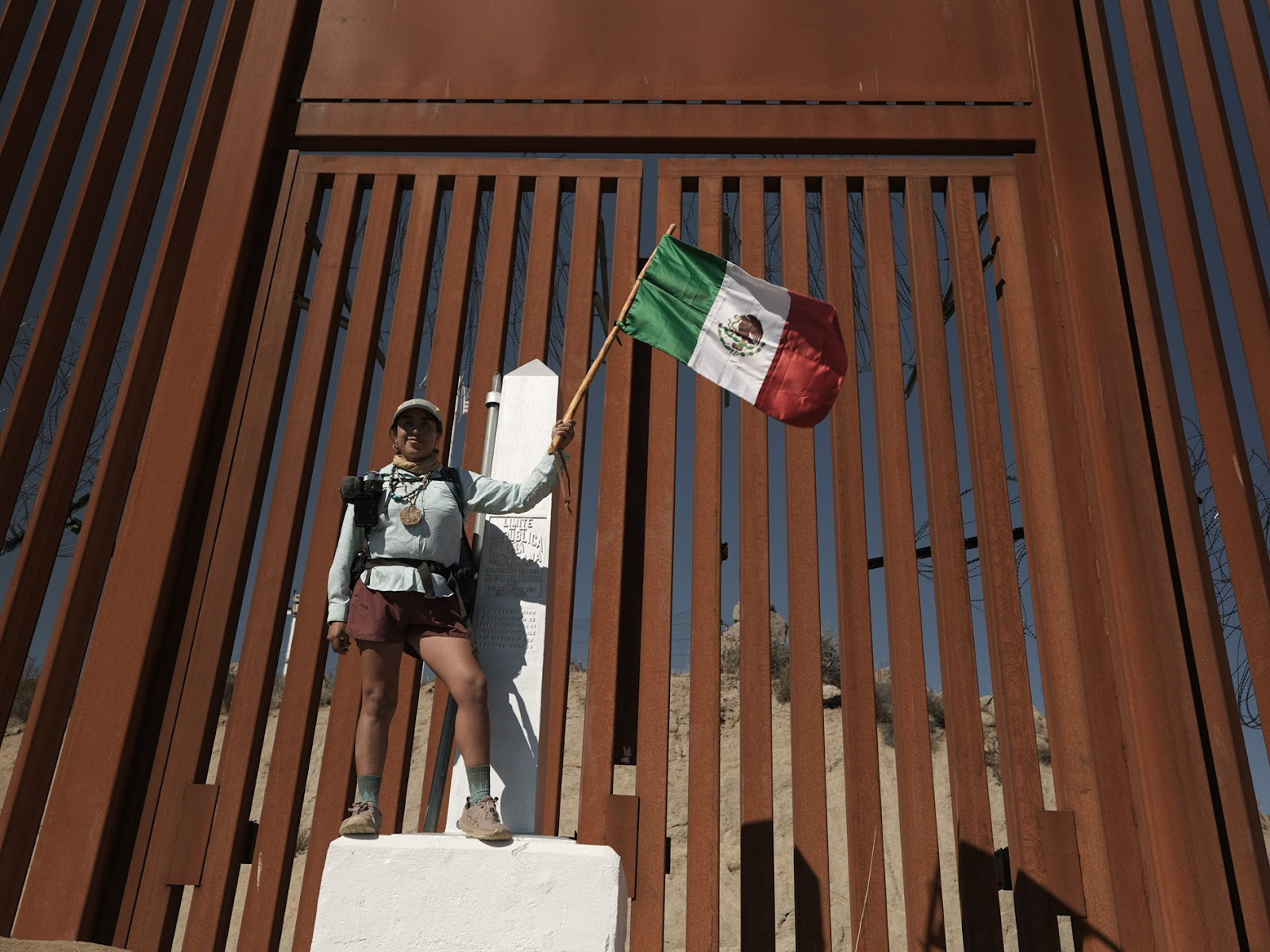Woman at Mexico-US border wall with Mexican flag standing triumphantly