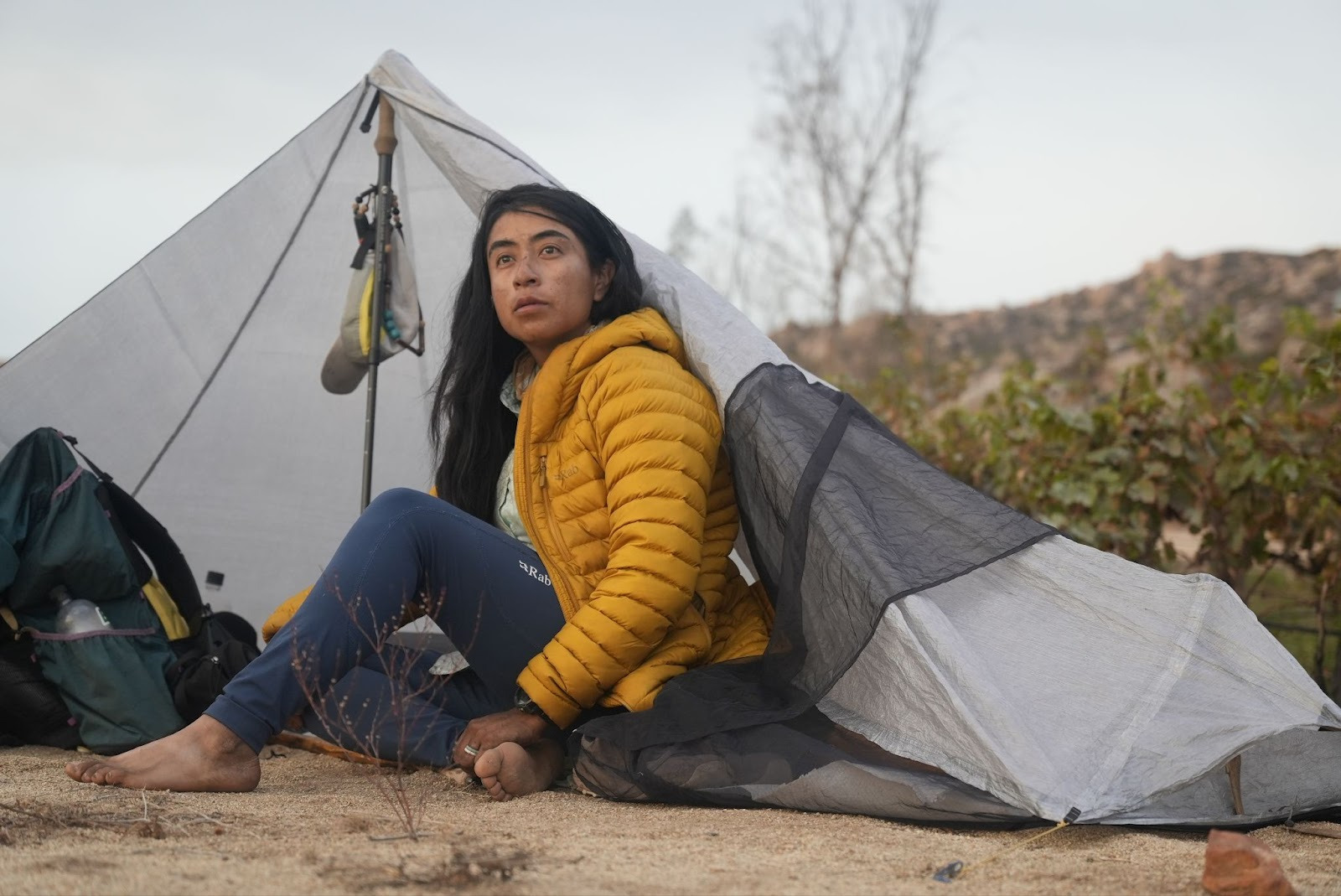 Woman sitting in front of ultralight trekking pole tent, looking into distance