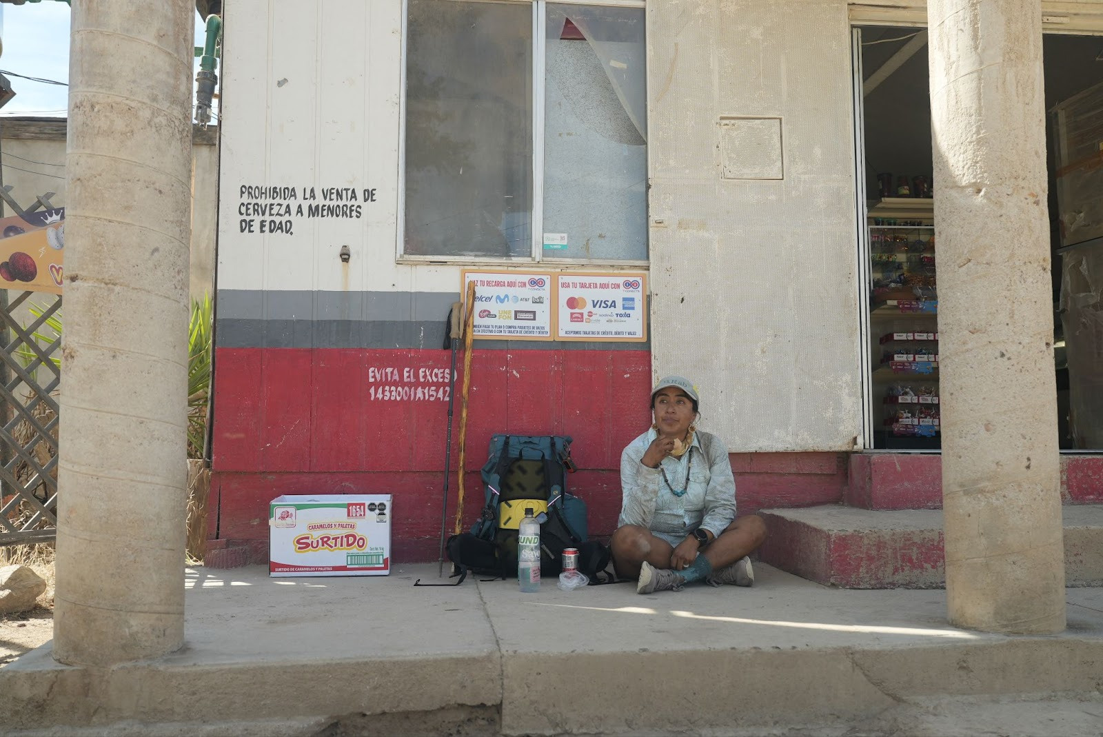 Woman eating a snack with camping gear beside her outside of a tienda 