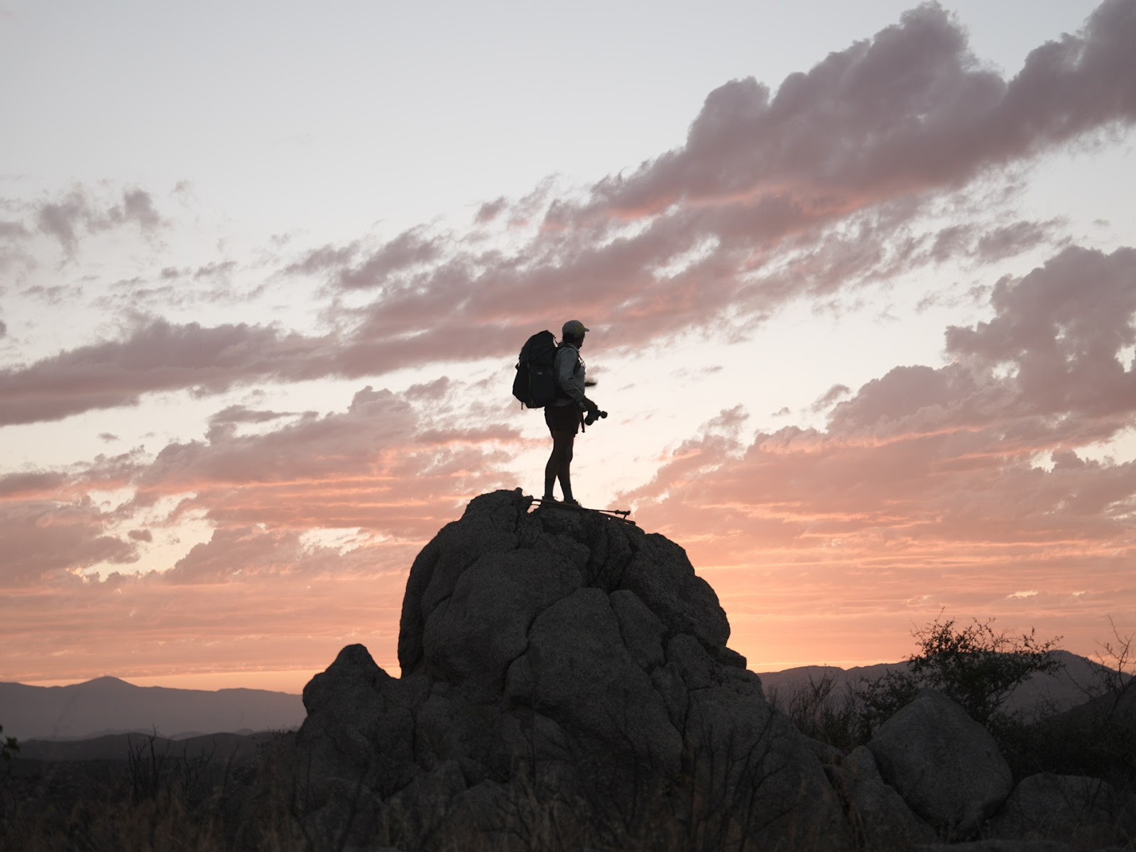 Woman standing on a large boulder in the desert at sunset