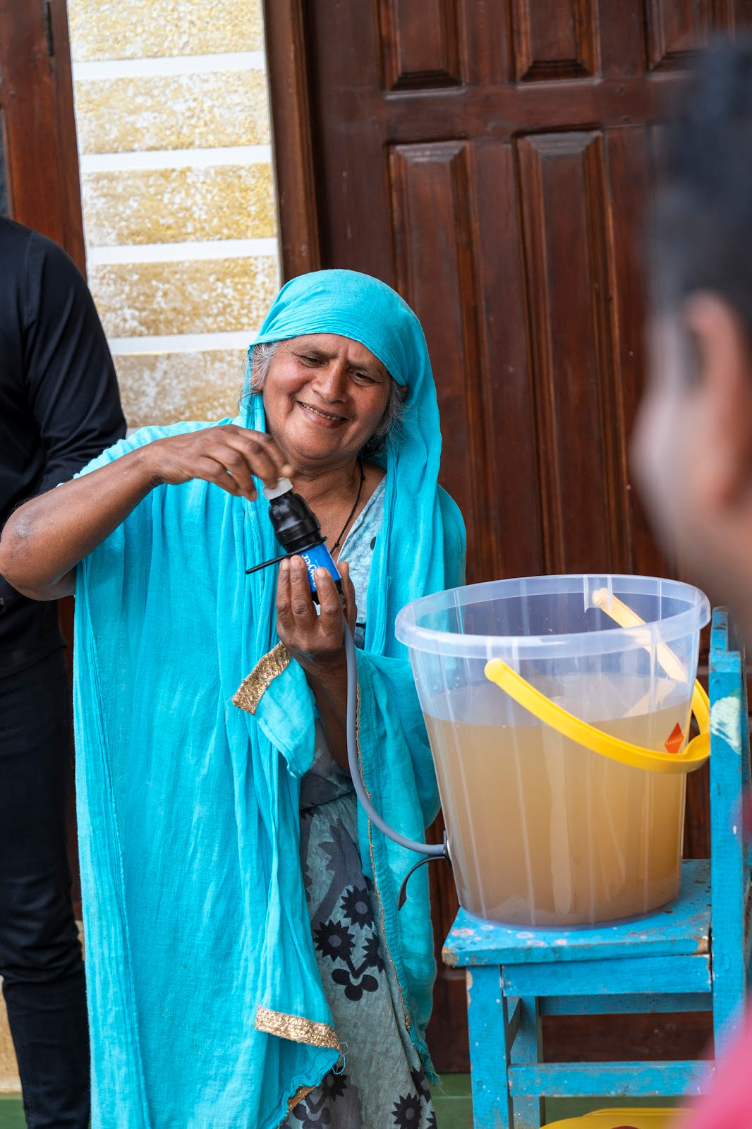 Woman smiling as she puts a cap back on a sawyer filter attached to a bucket system after learning backflushing maintenance