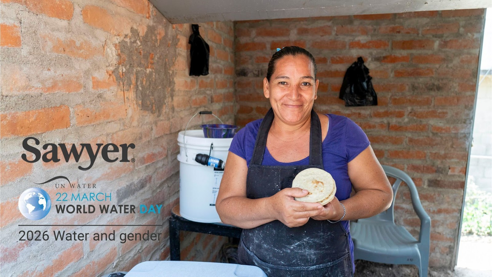 a woman smiles at the camera posing with tortillas with a sawyer bucket filtration system in the background