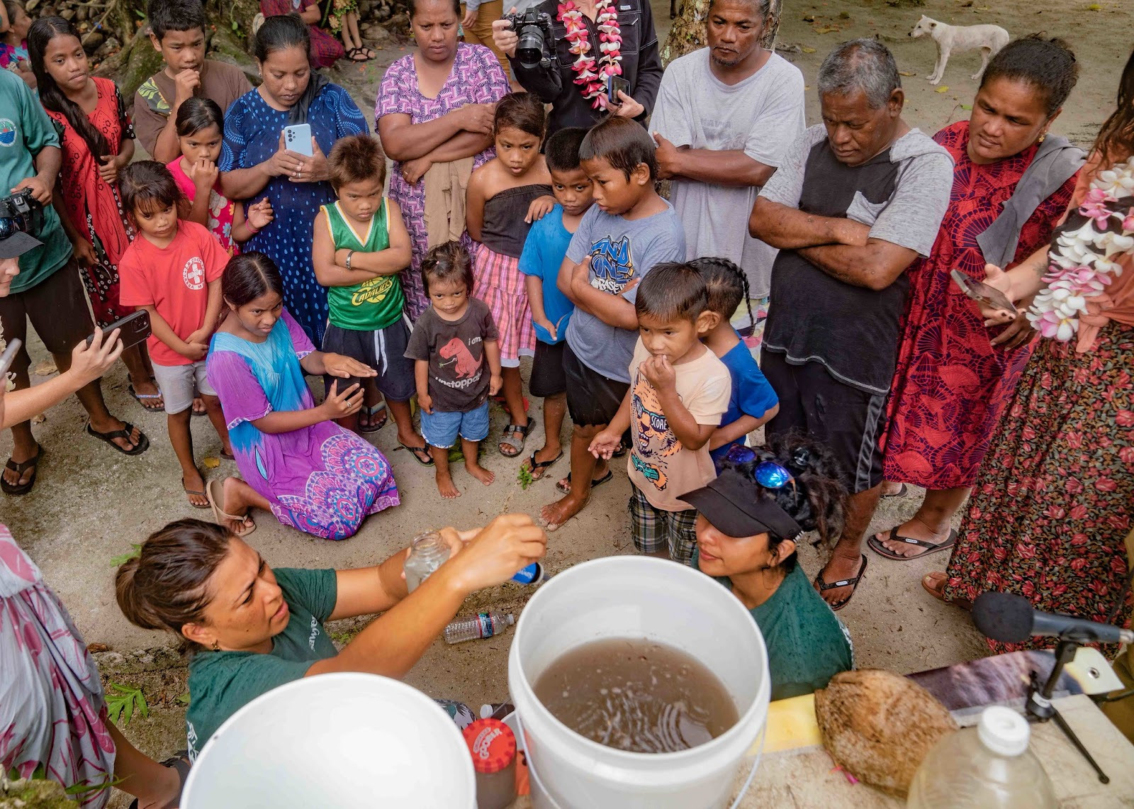 a woman demonstrates sawyer bucket filtration systems for a crowd with visibly dirty water