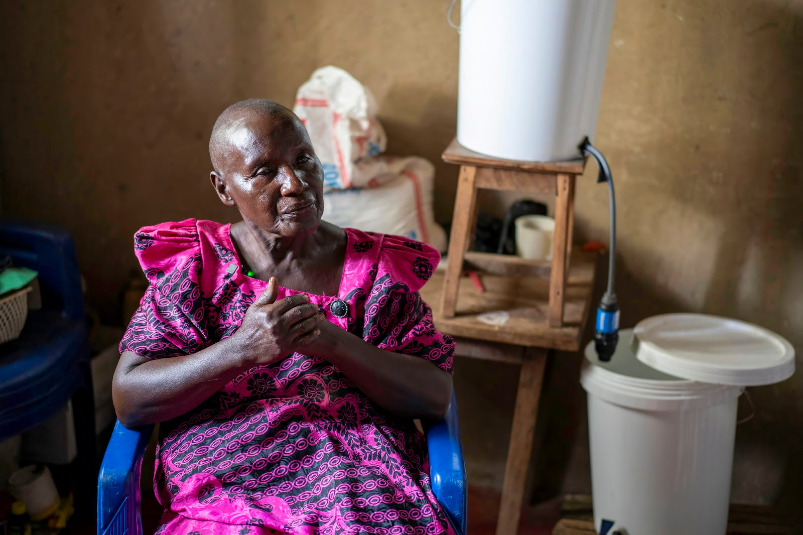 Woman sits in chair contemplatively with bucket system in background