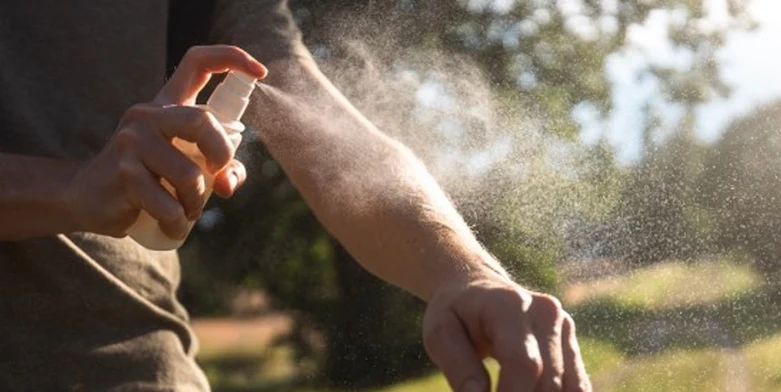 A person spraying bug repellent on their arm.