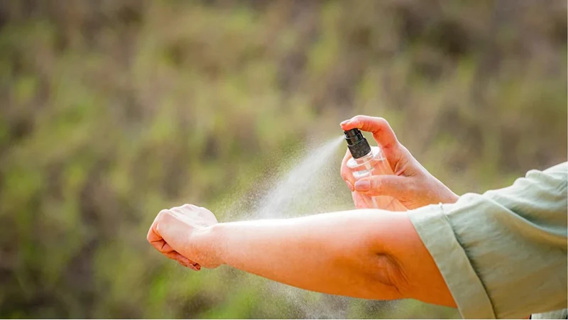 A person spraying bug repellent on their arm.