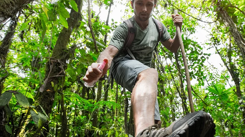 A man spraying his leg with insect repellent.