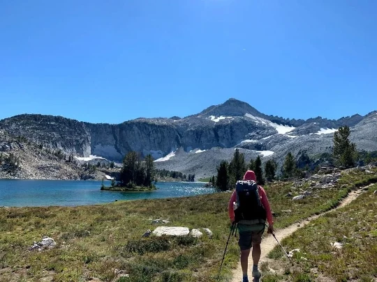A person hiking by a lake and mountains.